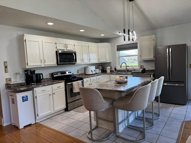 kitchen featuring appliances with stainless steel finishes, white cabinets, recessed lighting, a breakfast bar, and lofted ceiling