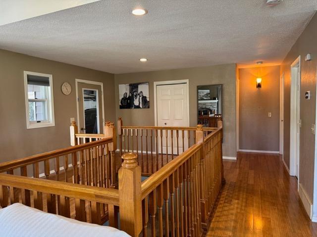 hallway with an upstairs landing, hardwood / wood-style floors, a textured ceiling, baseboards, and recessed lighting