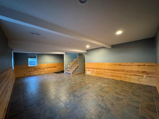 below grade area with wooden walls, a wainscoted wall, stairs, and recessed lighting