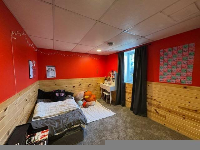 carpeted bedroom with wood walls, a wainscoted wall, and a paneled ceiling