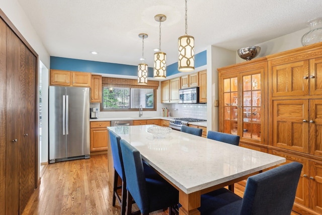 7676 Woodview Ct, Edina, MN 55439 - kitchen with stainless steel appliances, a sink, a breakfast bar, backsplash, and light wood-style floors