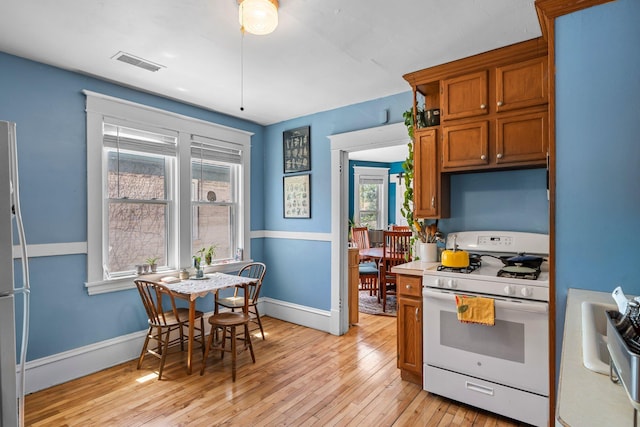 1123 5th St NE, Minneapolis, MN 55413 - kitchen featuring white appliances, brown cabinets, light wood-style floors, baseboards, and light countertops