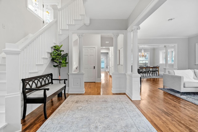 entrance foyer featuring wood finished floors, stairway, decorative columns, and ornamental molding
