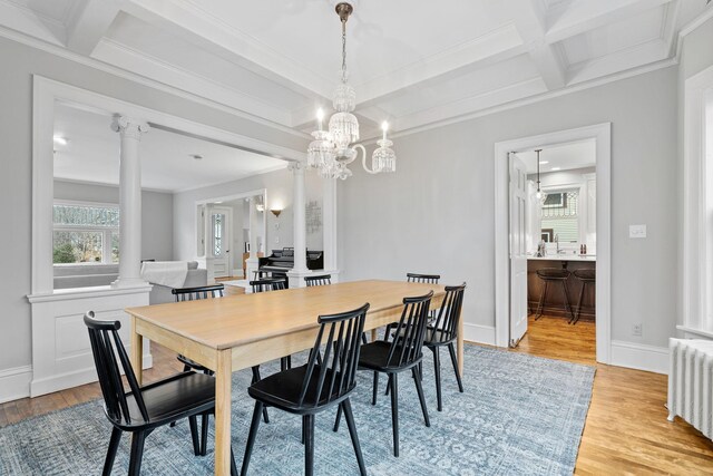dining room with radiator heating unit, decorative columns, coffered ceiling, light wood-style floors, and crown molding