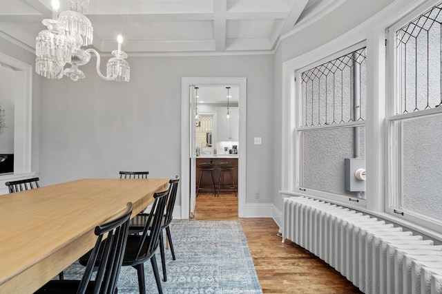 dining area with radiator heating unit, wood finished floors, beamed ceiling, ornamental molding, and coffered ceiling