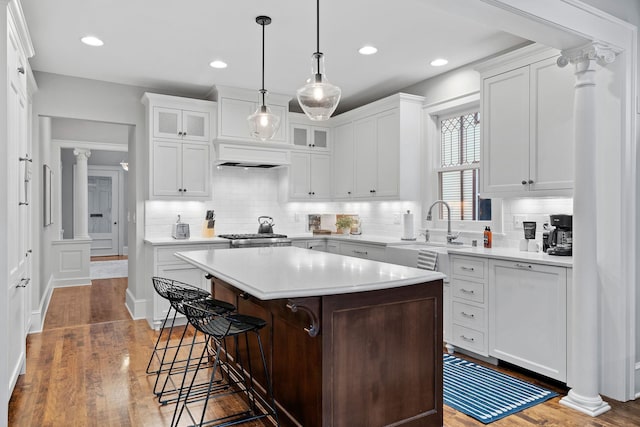kitchen with a kitchen bar, light countertops, tasteful backsplash, a center island, and wood finished floors