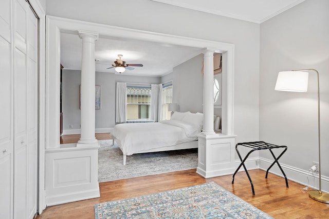 bedroom featuring ornate columns, wood finished floors, baseboards, ornamental molding, and ceiling fan
