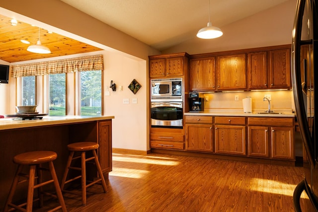 kitchen with stainless steel appliances, vaulted ceiling, brown cabinets, light countertops, and pendant lighting