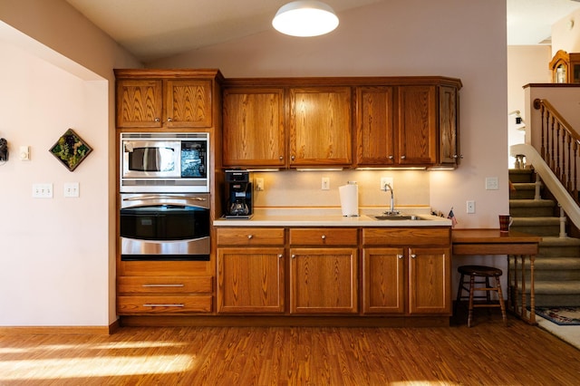 kitchen featuring appliances with stainless steel finishes, a sink, dark wood finished floors, brown cabinets, and vaulted ceiling