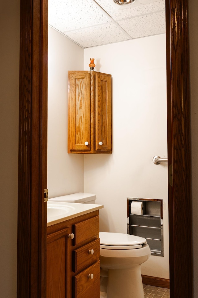 half bathroom featuring vanity, a drop ceiling, toilet, and tile patterned flooring
