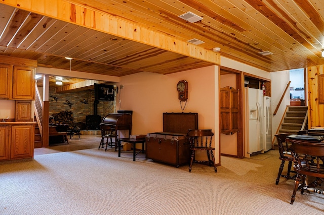 living area featuring stairway, a wood stove, light colored carpet, and wood ceiling