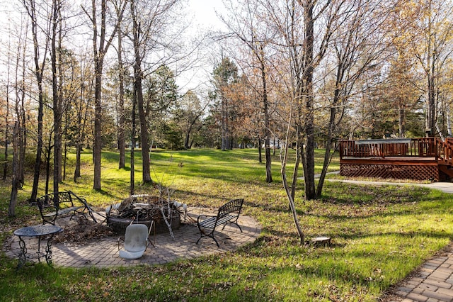 view of green lawn with an outdoor fire pit, a deck, and a patio area