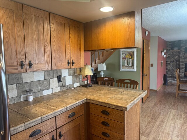 7525 Filbert Ln NE, Turtle River Twp, MN 56601 - kitchen with brown cabinets, a peninsula, light wood-style flooring, tasteful backsplash, and tile countertops