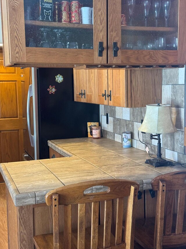 7525 Filbert Ln NE, Turtle River Twp, MN 56601 - kitchen featuring brown cabinetry, backsplash, tile counters, and freestanding refrigerator