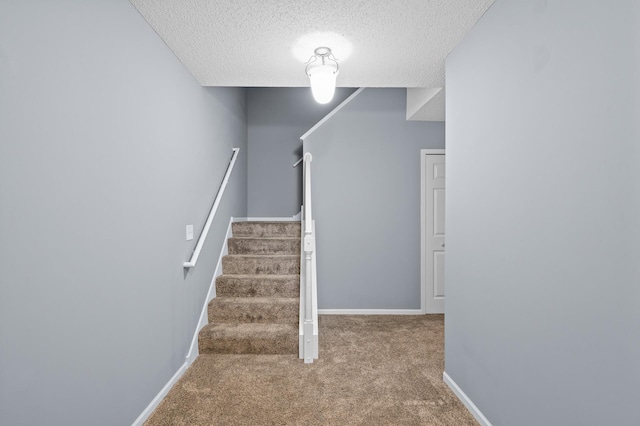 stairway with carpet flooring, a textured ceiling, and baseboards