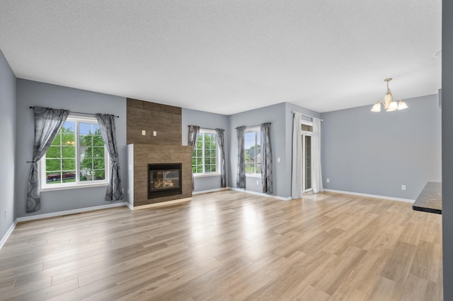 unfurnished living room featuring a chandelier, plenty of natural light, a textured ceiling, and light wood-style flooring