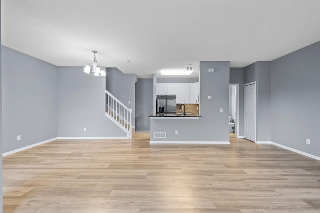 unfurnished living room featuring a sink, a chandelier, light wood-type flooring, and baseboards