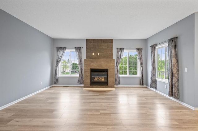 unfurnished living room featuring healthy amount of natural light, light wood-type flooring, and a tile fireplace