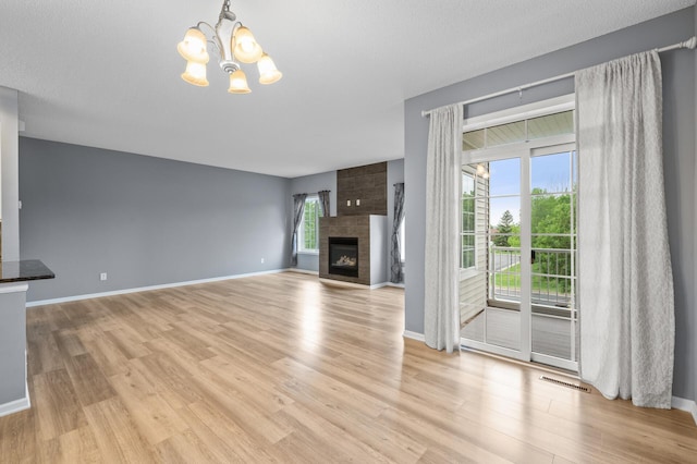 unfurnished living room featuring a chandelier, light wood-style floors, a fireplace, and baseboards