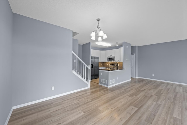 unfurnished living room featuring a chandelier, light wood-type flooring, stairway, and baseboards