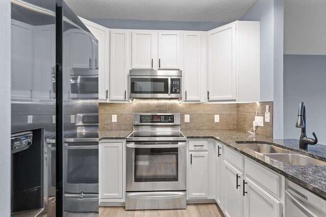 kitchen featuring appliances with stainless steel finishes, a sink, dark stone counters, white cabinets, and a textured ceiling