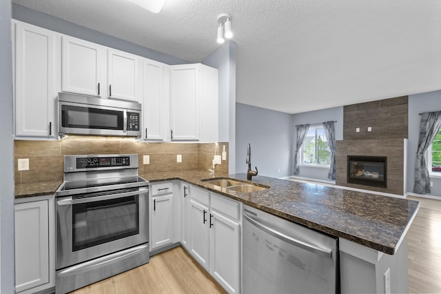kitchen with stainless steel appliances, a sink, a peninsula, open floor plan, and dark stone counters