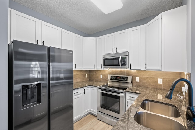 kitchen featuring appliances with stainless steel finishes, a sink, dark stone countertops, white cabinetry, and a textured ceiling
