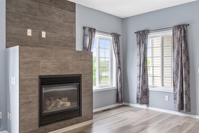 detailed view of wood finished floors, a tile fireplace, and baseboards