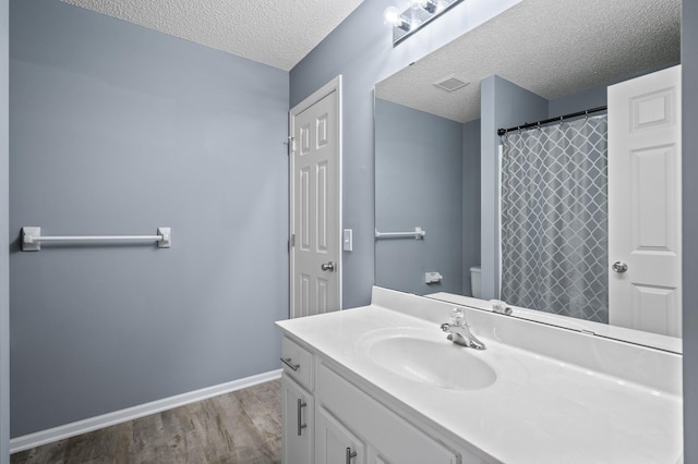 full bathroom with wood finished floors, toilet, a textured ceiling, vanity, and baseboards
