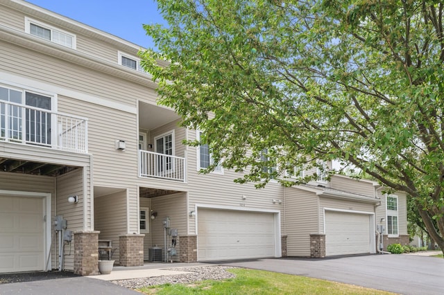 view of front of house with central air condition unit, asphalt driveway, brick siding, and a garage