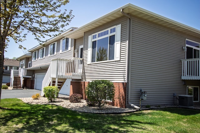 view of home's exterior featuring a garage, central AC unit, stairs, a yard, and brick siding