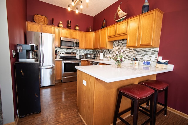kitchen with stainless steel appliances, a peninsula, tasteful backsplash, light countertops, and dark wood finished floors
