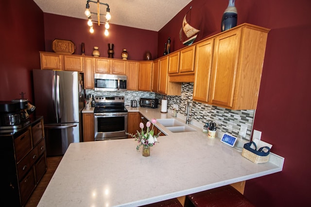kitchen with stainless steel appliances, a sink, a peninsula, decorative backsplash, and light countertops