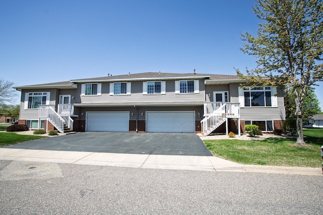 bi-level home featuring stairs, an attached garage, asphalt driveway, and a front yard