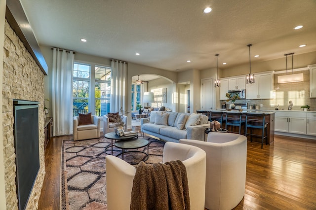 17796 Junelle Ct, Lakeville, MN 55044 - living area with recessed lighting, a stone fireplace, dark wood-style flooring, a textured ceiling, and arched walkways