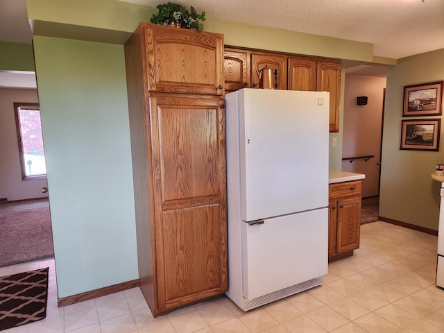 kitchen with freestanding refrigerator, brown cabinets, light countertops, baseboards, and light floors