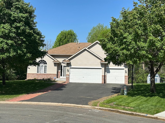 view of property hidden behind natural elements featuring an attached garage, brick siding, asphalt driveway, and a front yard