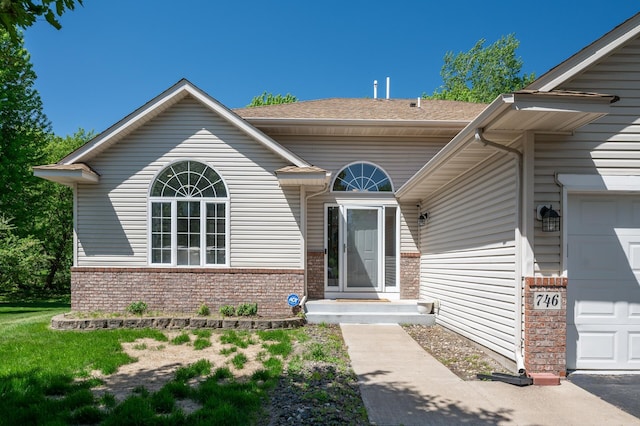 property entrance featuring brick siding, an attached garage, and roof with shingles