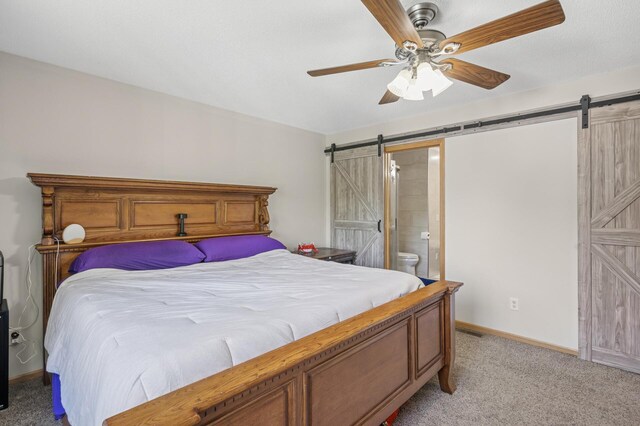 bedroom featuring a barn door, light carpet, ensuite bath, and a ceiling fan
