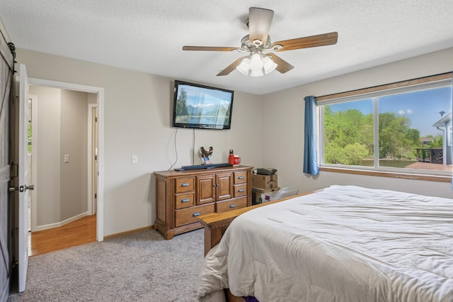 bedroom featuring light carpet, a textured ceiling, baseboards, ceiling fan, and a barn door