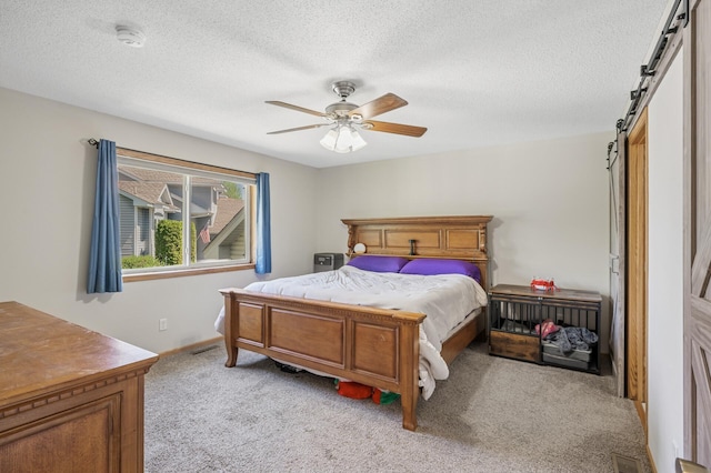 bedroom with light carpet, a barn door, a textured ceiling, a ceiling fan, and baseboards