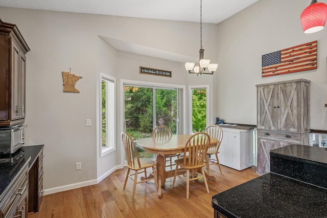 dining room with light wood finished floors, a chandelier, baseboards, and a high ceiling