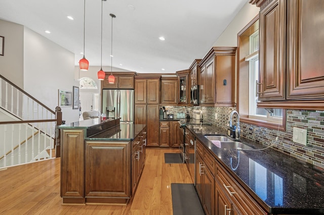 kitchen with a sink, stainless steel appliances, light wood-style flooring, a center island, and decorative light fixtures