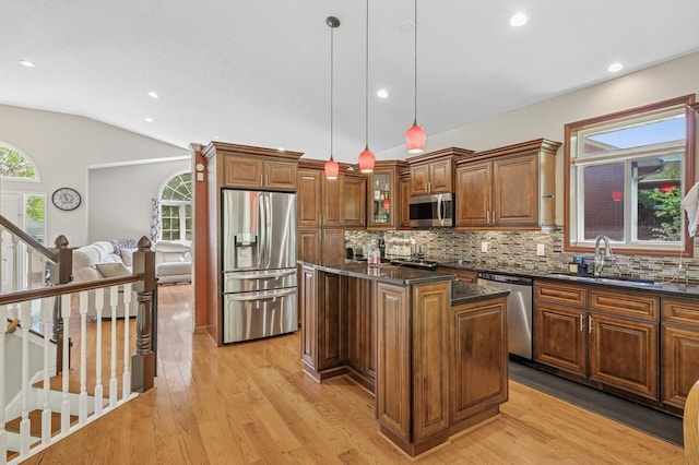 kitchen featuring appliances with stainless steel finishes, a sink, a kitchen island, backsplash, and light wood finished floors
