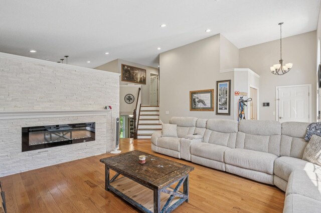 living area featuring a stone fireplace, wood finished floors, a chandelier, stairs, and recessed lighting