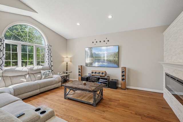 living area featuring vaulted ceiling, light wood-type flooring, a stone fireplace, baseboards, and recessed lighting