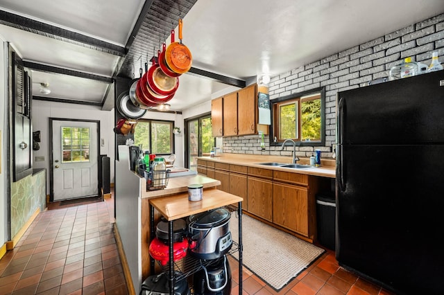 kitchen featuring freestanding refrigerator, a sink, light countertops, brown cabinets, and dark tile patterned flooring