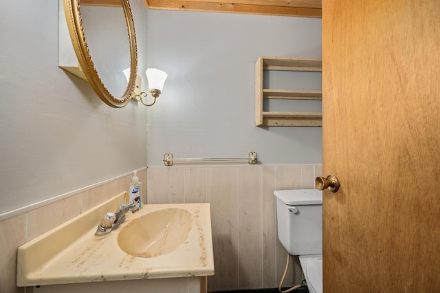 half bath featuring vanity, toilet, and wainscoting