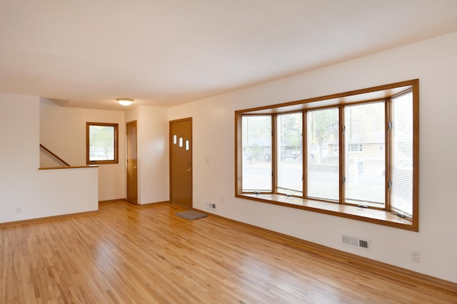 unfurnished living room with light wood-type flooring, baseboards, and stairway