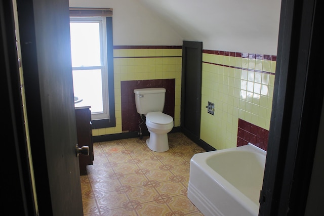 2612 3rd Ave W, Hibbing, MN 55746 - bathroom featuring tile walls, lofted ceiling, a tub, and wainscoting